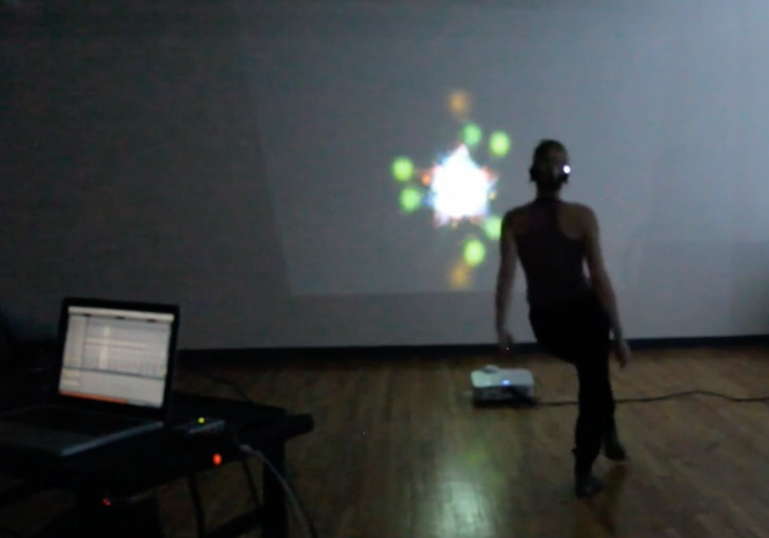A dark room with a dancer moving to trigger an on screen image of abstract shapes